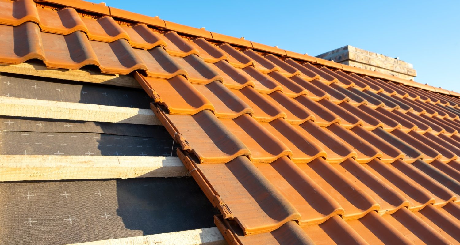 Overlapping rows of yellow ceramic roofing tiles mounted on wooden boards covering residential